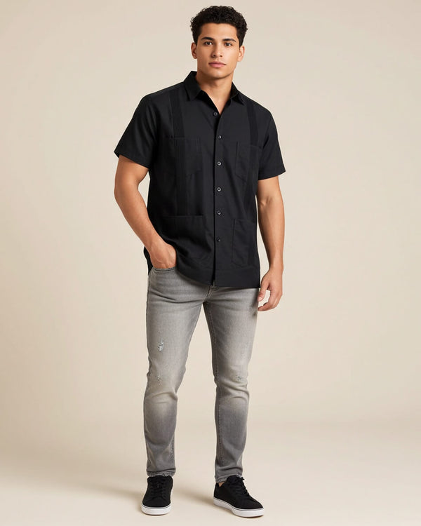 Man wearing a black short-sleeve button-up guayabera shirt and gray jeans on a beige background