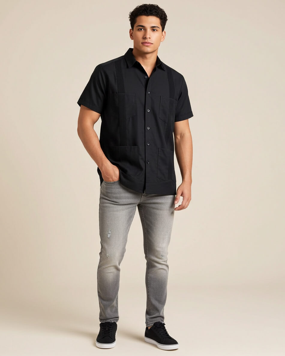 Man wearing a black short-sleeve button-up guayabera shirt and gray jeans on a beige background
