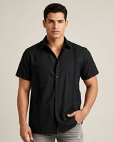 Man wearing a black short-sleeve guayabera shirt against a beige background