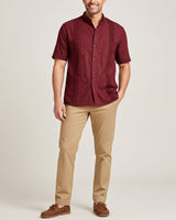 Man wearing a maroon short-sleeve guayabera shirt and beige pants on a plain background