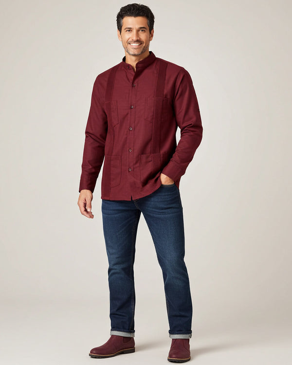 Man wearing a burgundy guayabera shirt and blue jeans on a plain background