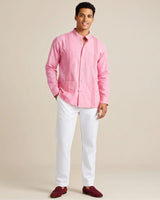 Man wearing a pink guayabera shirt and white pants on a beige background