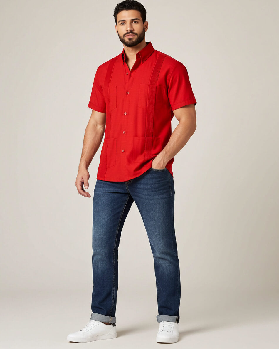 Man wearing a red guayabera shirt and blue jeans on a plain background