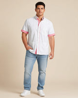 Man wearing a white guayabera shirt with pink accents and blue jeans on a beige background