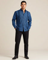 Man wearing a blue plaid shirt and black pants against a beige background