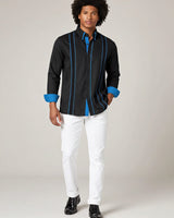Man wearing a black guayabera shirt with blue accents and white pants on a plain background