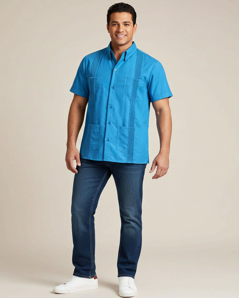 Man wearing a turquoise blue short-sleeve guayabera shirt and dark jeans on a beige background