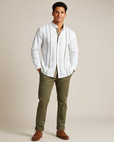 Man wearing a white guayabera shirt and green pants against a beige background