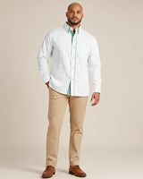 Man wearing a white guayabera shirt with a green accent collar, beige pants, and brown shoes on a beige background