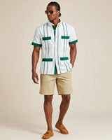 Man wearing a white guayabera shirt with green accents and beige shorts on a beige background