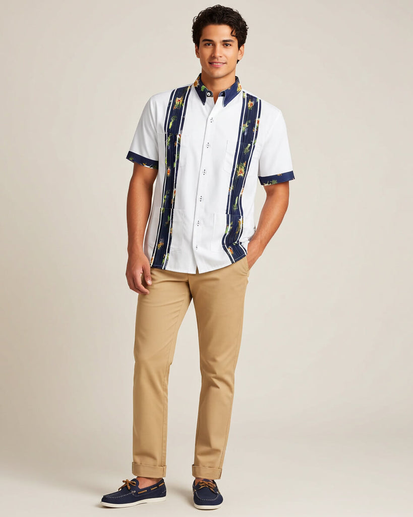 Man wearing a white guayabera shirt with blue accents and beige pants on a plain background