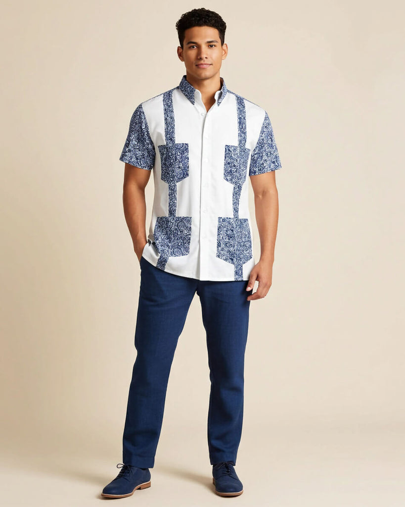 Man wearing a white guayabera shirt with paisley accents and blue pants on a beige background