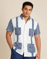 Man wearing a white guayabera shirt with blue paisley pockets against a beige background