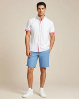 Man wearing a white guayabera shirt with pink accents and blue shorts on a beige background