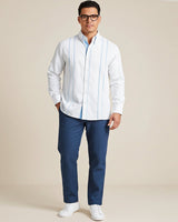 Man wearing a white guayabera long-sleeve shirt with sky blue accents and blue pants on a beige background