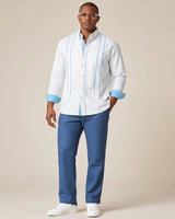 Man wearing a white guayabera shirt with blue accents and blue pants on a beige background