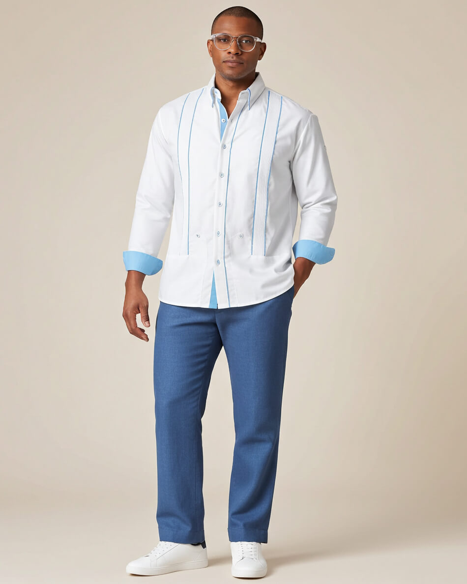 Man wearing a white guayabera shirt with blue accents and blue pants on a beige background