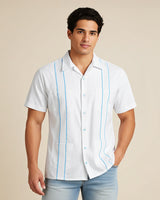 Man wearing a white guayabera short-sleeve shirt with sky blue accented pleats and light blue shorts on a beige background