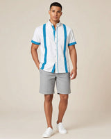 Man wearing a white guayabera shirt with turquoise stripes and gray shorts on a beige background