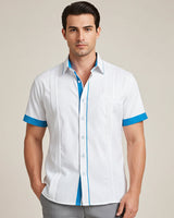 Man wearing a white guayabera shirt with turquoise accents on a beige background