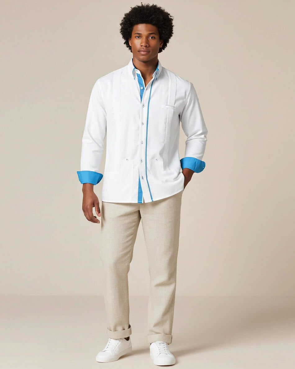 Man wearing a white guayabera shirt with turquoise accents and beige pants on a beige background