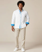 Man wearing a white guayabera shirt with turquoise accents and beige pants on a beige background