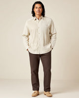 Man wearing a beige guayabera shirt and brown pants against a plain background