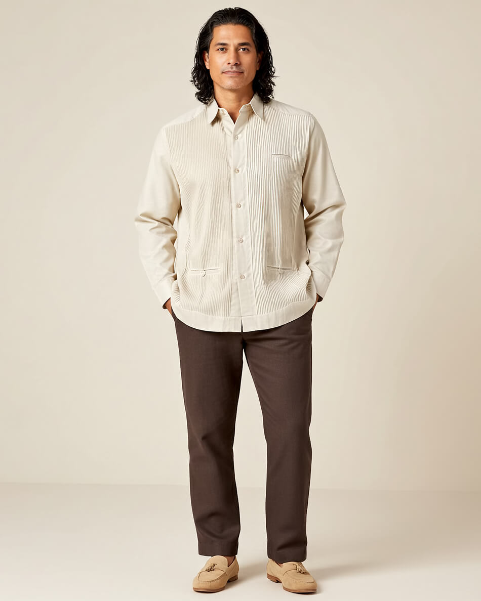 Man wearing a beige guayabera shirt and brown pants against a plain background