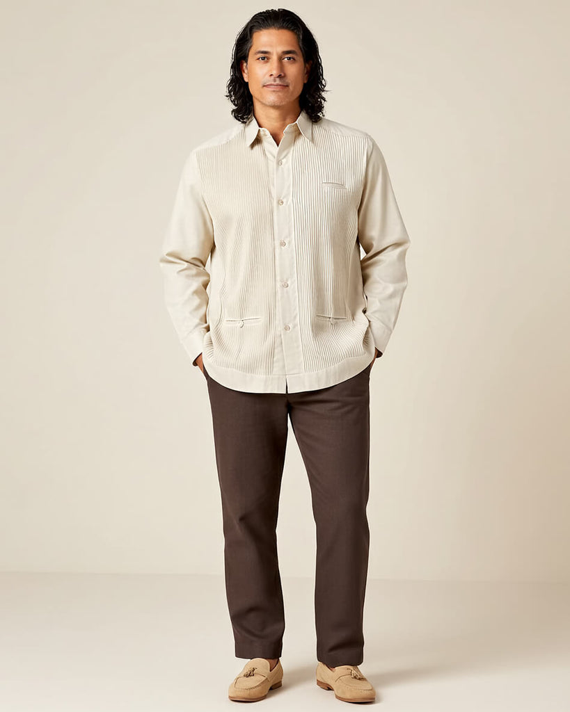 Man wearing a beige guayabera shirt and brown pants against a plain background