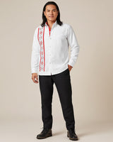 Man wearing a white guayabera red embroidered shirt with black pants on a beige background