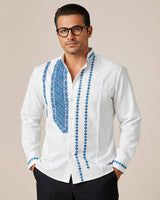 Man wearing a white guayabera shirt with blue embroidery on a beige background