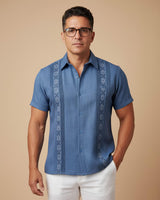 Man wearing a blue embroidered guayabera shirt against a beige background