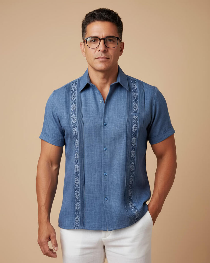 Man wearing a blue embroidered guayabera shirt against a beige background