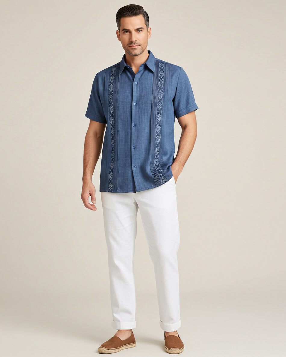 Man wearing a blue embroidered guayabera shirt with white pants on a beige background