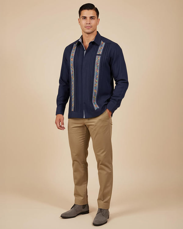 Man wearing a navy embroidered guayabera shirt with beige pants on a beige background