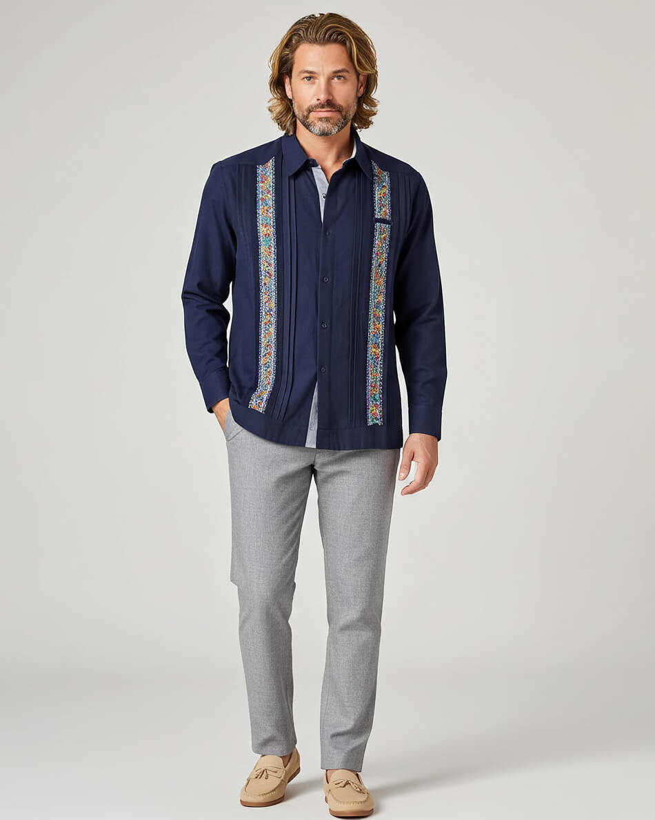 Man wearing a navy guayabera shirt with colorful patterns and gray pants on a white background