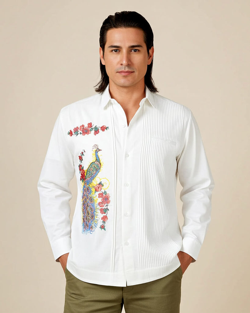 Man wearing a white embroidered guayabera peacock shirt with a colorful design, green pants, and brown shoes on a beige background.