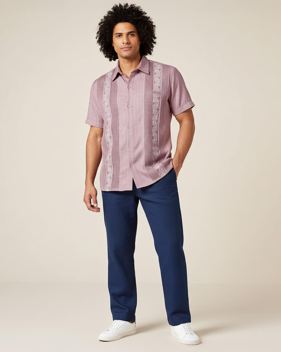 Man wearing a pink patterned guayabera shirt and blue pants on a beige background