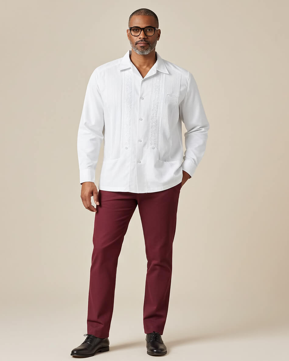 Man wearing a white guayabera shirt and maroon pants against a beige background