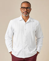 Man wearing a white nortena guayabera shirt and maroon pants against a beige background