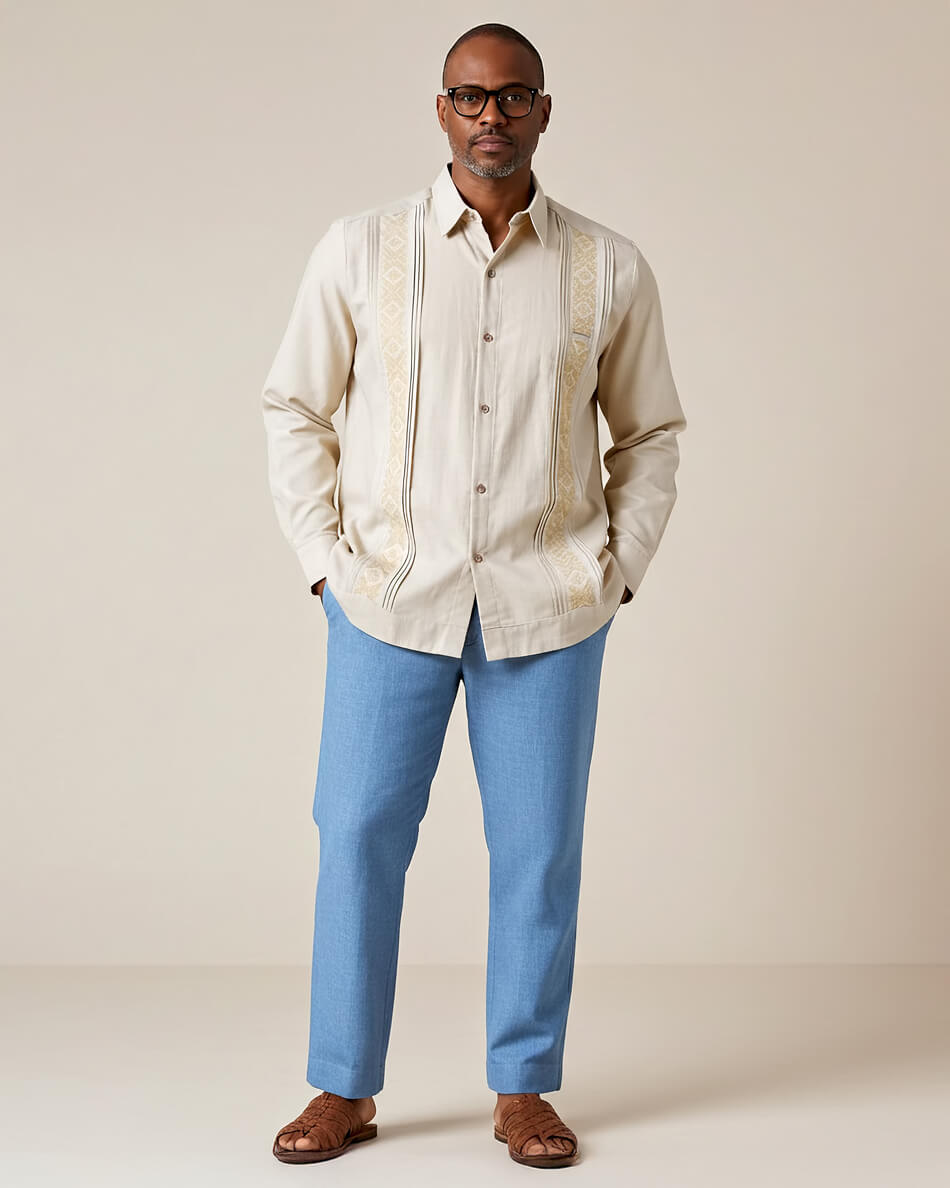 Man wearing a beige guayabera shirt with striped pattern and blue pants against a plain background