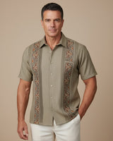 Man wearing a patterned khaki guayabera shirt with tan pants on a beige background
