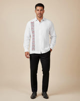 Man wearing a white embroidered guayabera shirt with black pants on a beige background