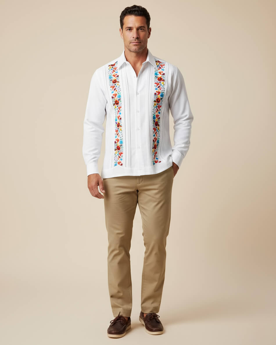 Man wearing a white embroidered guayabera shirt with colorful patterns and beige pants on a beige background