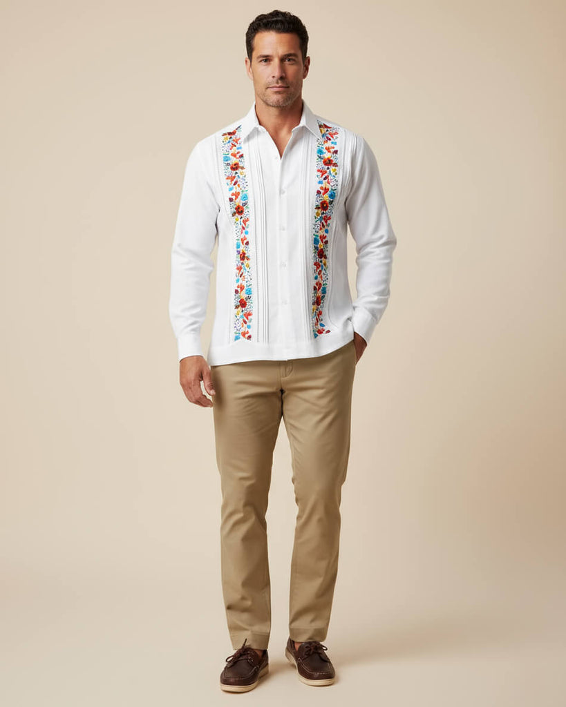 Man wearing a white embroidered guayabera shirt with colorful patterns and beige pants on a beige background