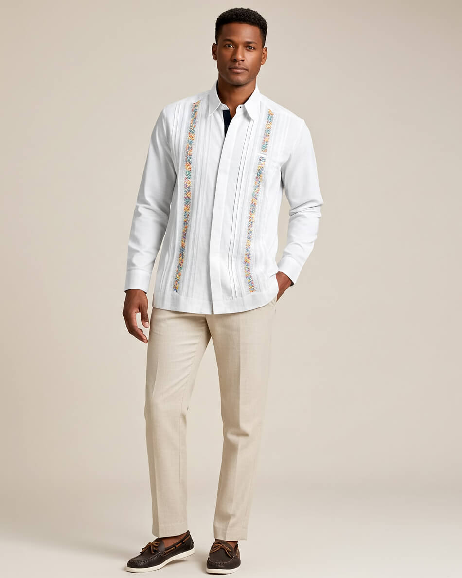 Man wearing a white guayabera rainbow embroidered shirt and beige pants against a neutral background
