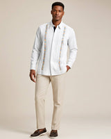 Man wearing a white guayabera rainbow embroidered shirt and beige pants against a neutral background