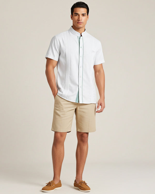 Man wearing a white short-sleeve guayabera shirt and beige shorts against a plain background