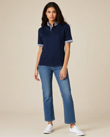 Woman wearing a navy blue polo shirt and jeans on a beige background